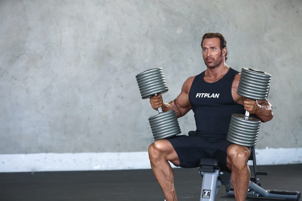 A man holding dumbbells and sitting on a bench.