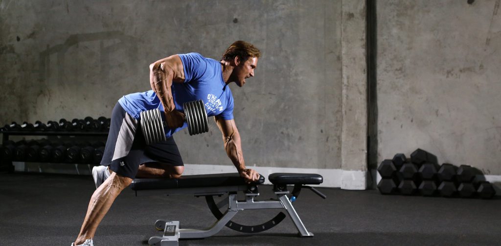 A man doing dumbbell rows in a gym.