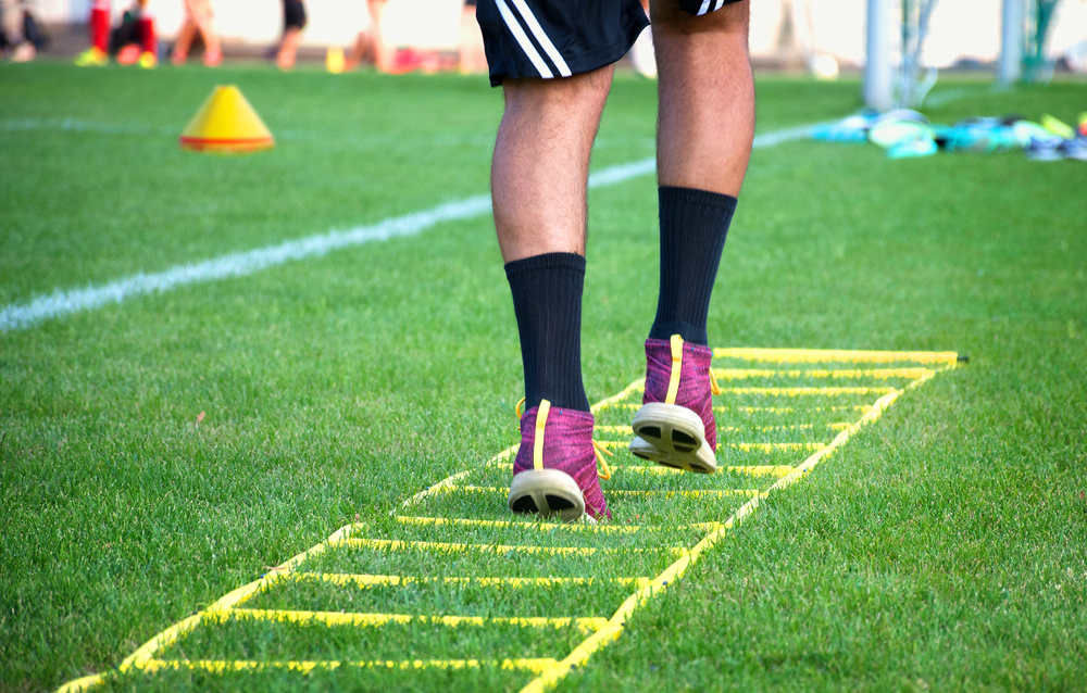 A person running on a speed ladder in a field.