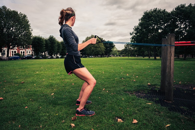 A woman in a park exercising with a resistance band.