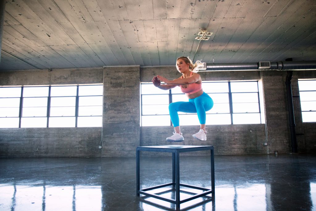 A woman doing box jumps in a gym.