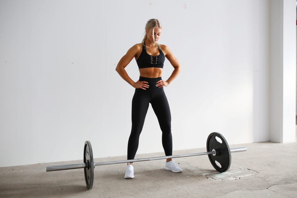 A woman standing next to a barbell in a gym.