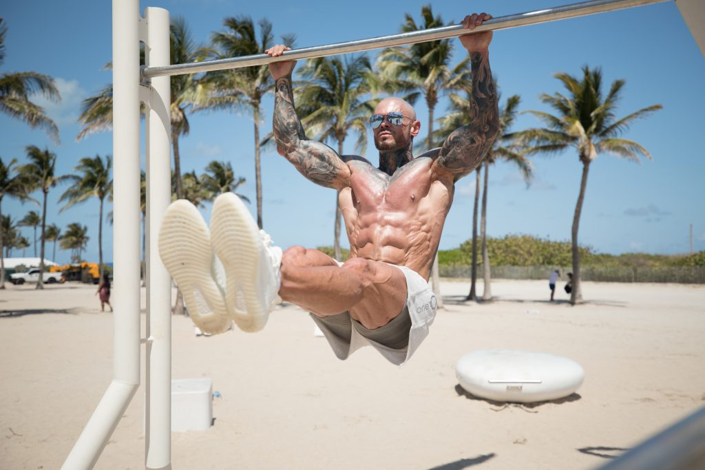 A man doing L-sit pull-ups at a beach.